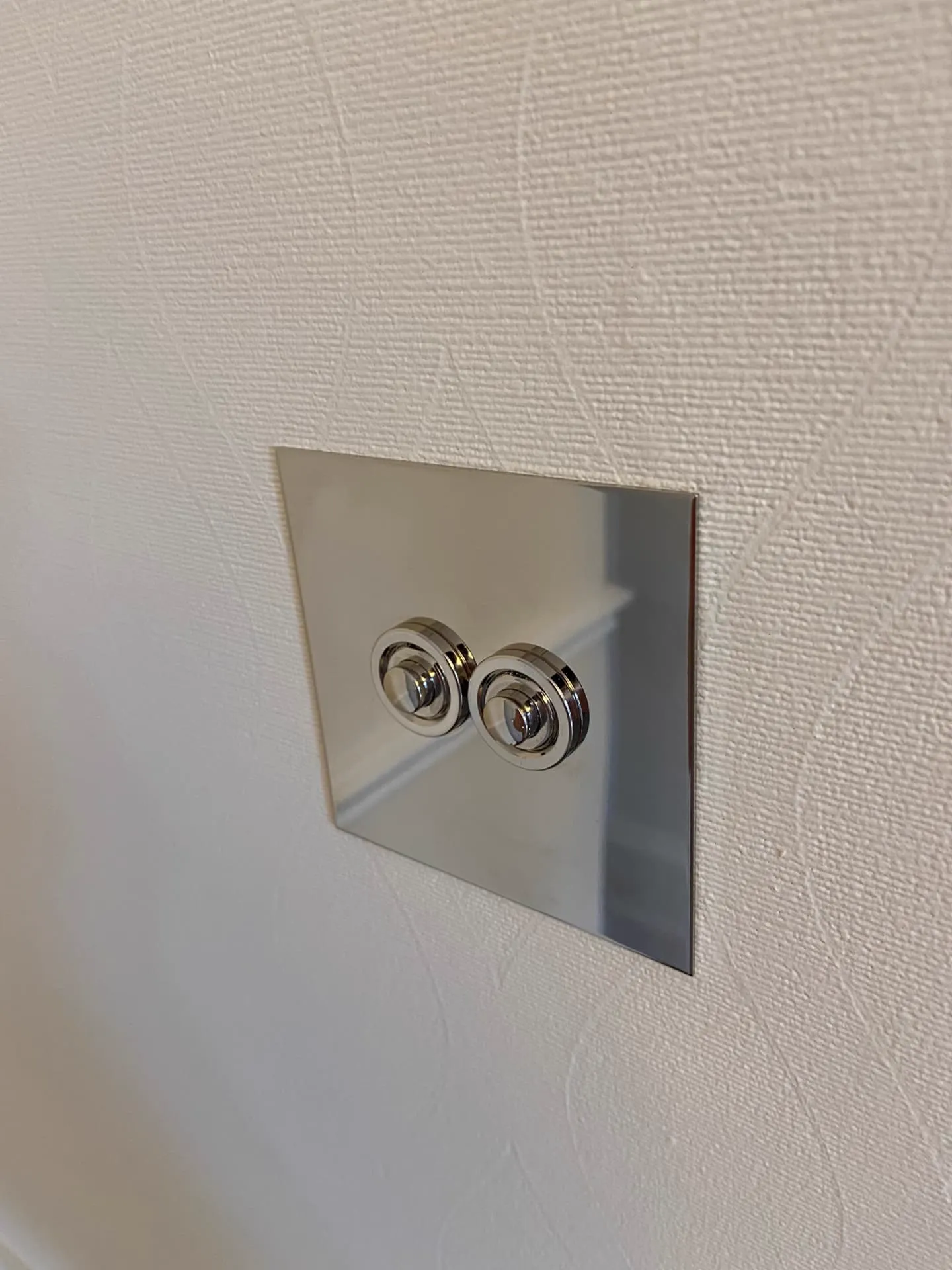 Polished steel double toggle light switch plate fitted on a cream wall, electrical work in Belgravia by coreMaint